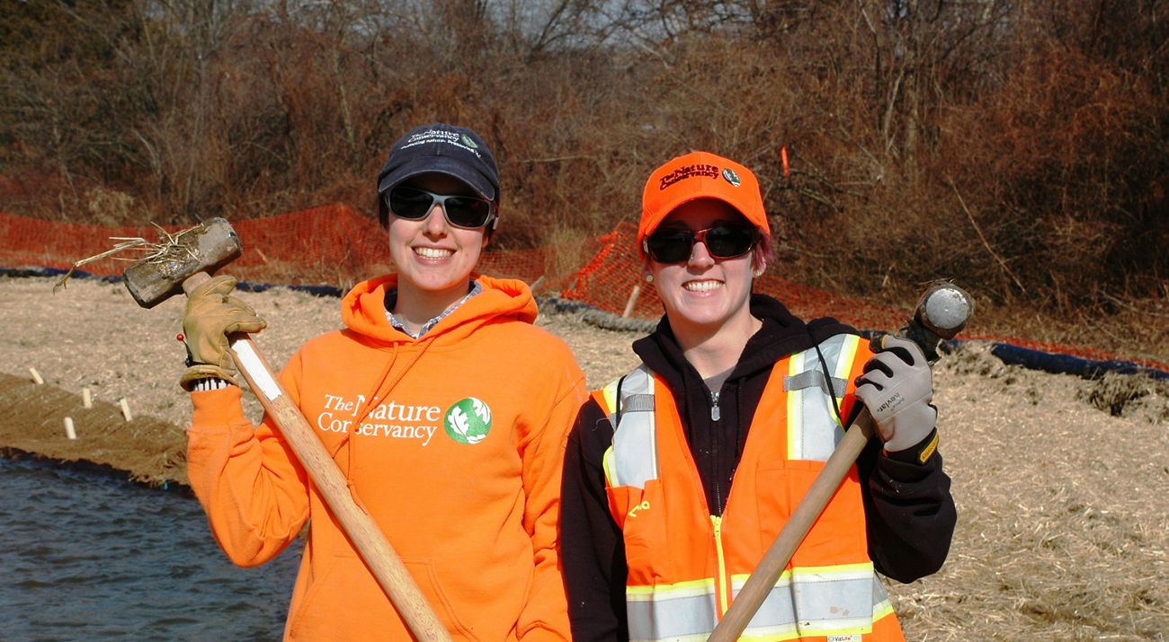 Two volunteers in bright orange vests holding sledge hammers.