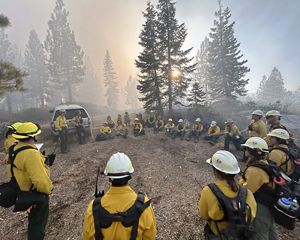 A group of people sit in a circle during a prescribed burn. 
