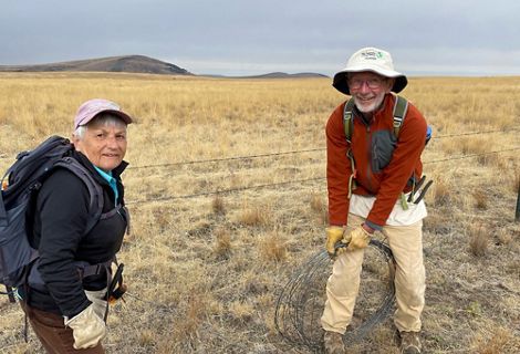 Dale and Lois Derouin stand on an open grassland and remove barbed-wire fencing.