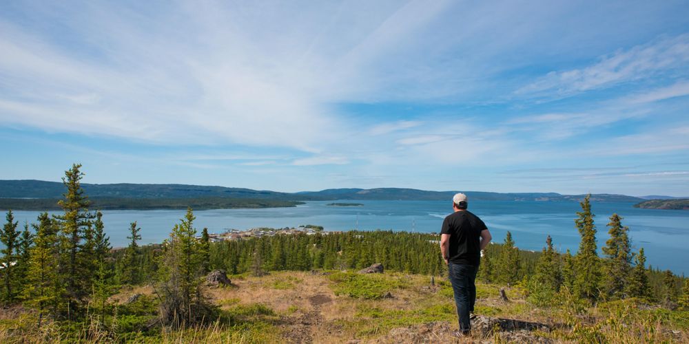 A man looks out at water and trees while standing on a high vantage point.