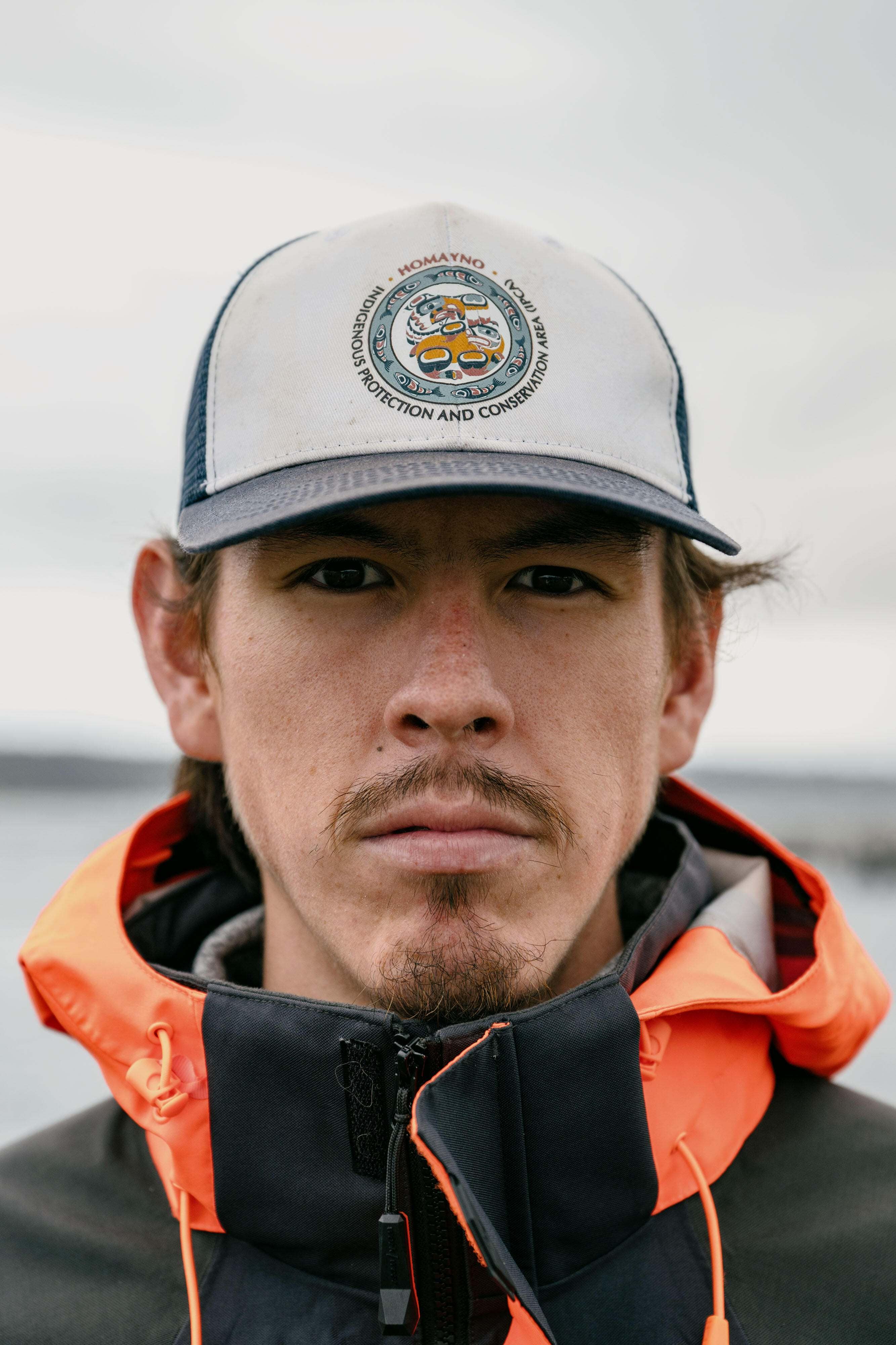 Portrait of Payton Wilson-Wells, a Wei Wai Kum Guardian, wearing a hat with the logo of the Homayno (Heydon) Bay restoration project, in Campbell River, Canada.
