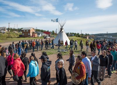 Dozens of people form a large circle, with a teepee in the background.