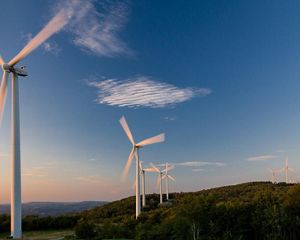 Wind turbines in motion stand atop forested hills.